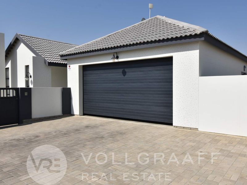Modern residential garage featuring a dark automated door, tiled roof, and a neat paved driveway with secure boundary walling.
