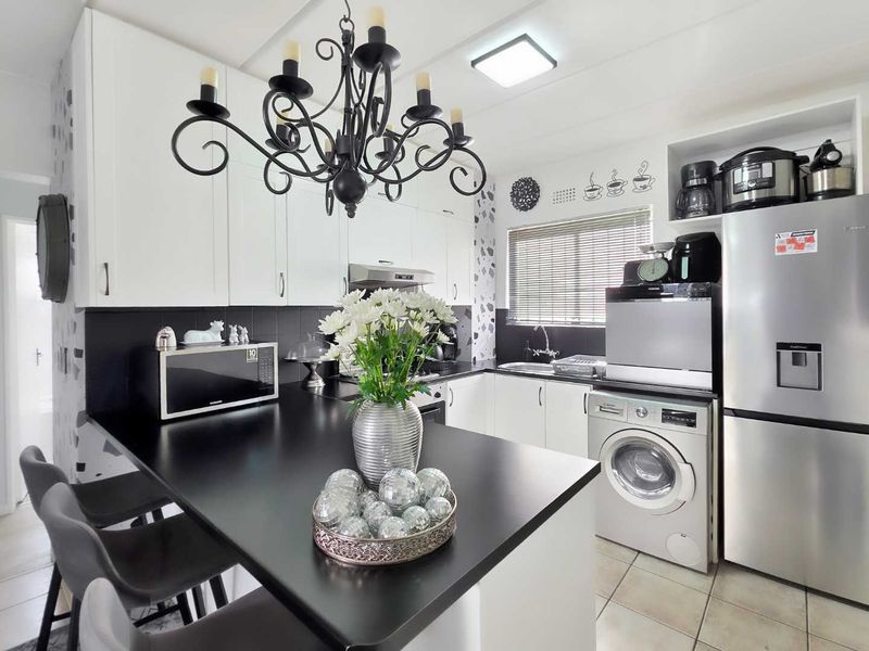 Modern kitchen featuring white cabinetry, contrasting black countertops, integrated appliances, and a breakfast bar area with contemporary lighting.