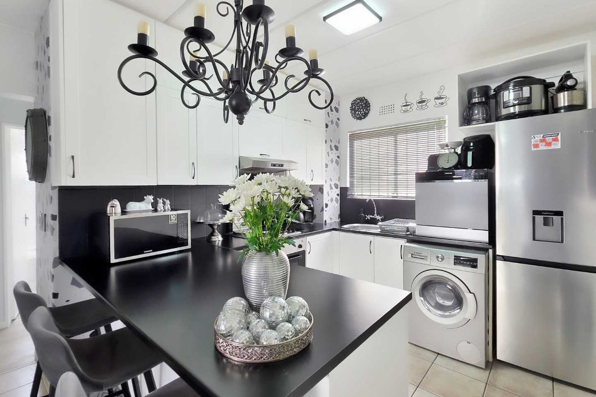 Modern kitchen featuring white cabinetry, contrasting black countertops, integrated appliances, and a breakfast bar area with contemporary lighting.