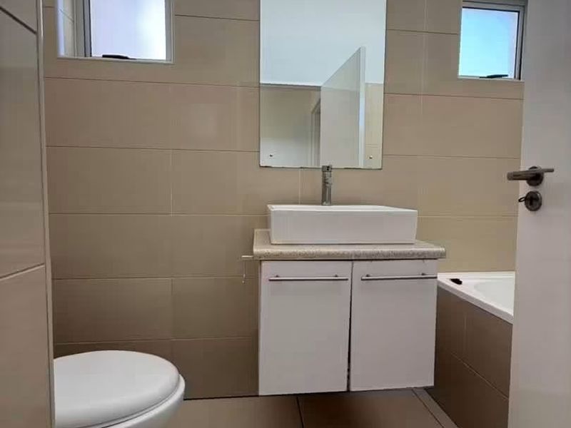 A clean, modern bathroom featuring a wall-mounted vanity with a vessel sink, neutral ceramic tiling, and a built-in bathtub.