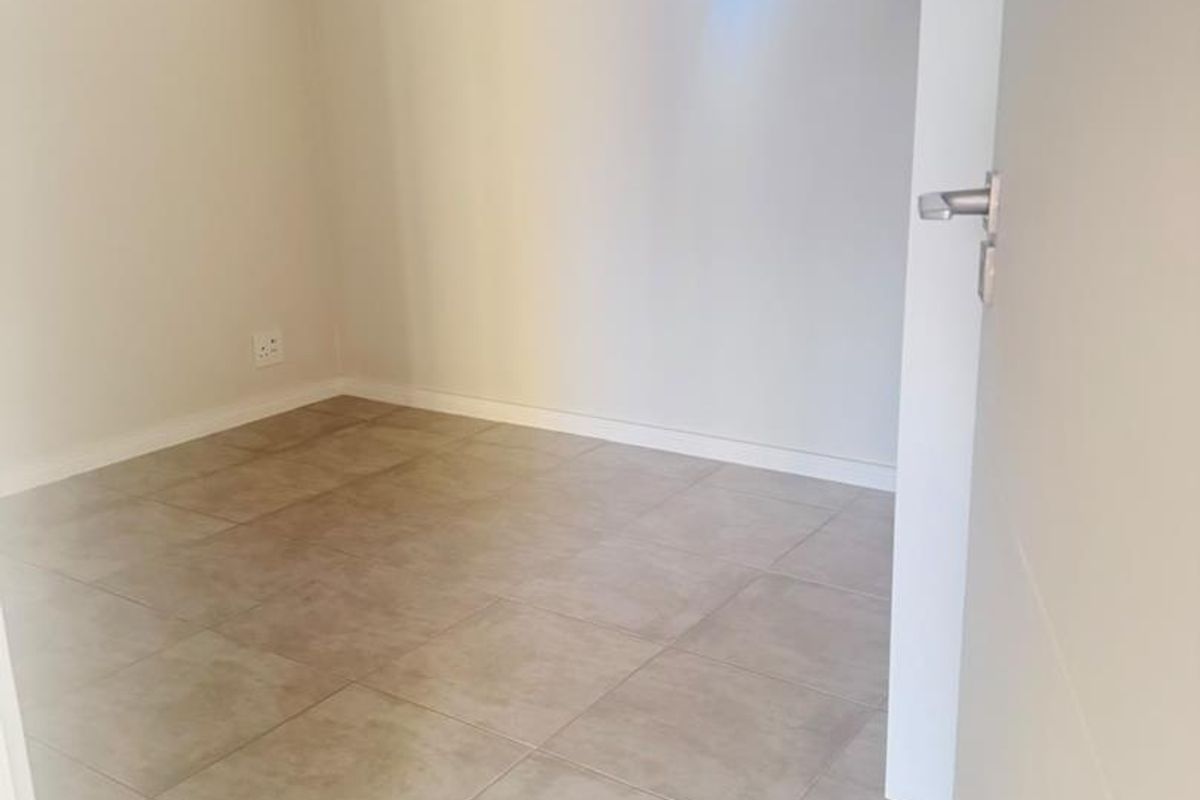 A bright, empty bedroom featuring neutral tiled flooring and a high-level clerestory window, offering a clean and versatile space ready for personalization.