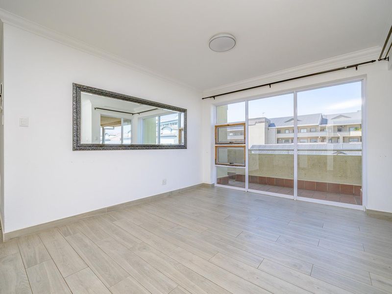 Bright and spacious living area featuring modern laminate flooring, large sliding glass doors leading to a balcony, and neutral finishes throughout.
