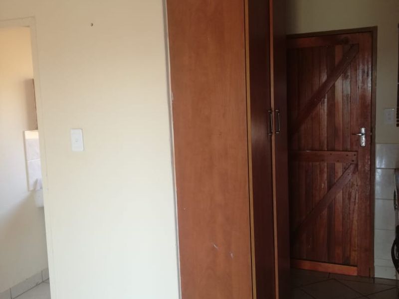 A functional hallway featuring tiled flooring, a built-in wooden cupboard, and a solid timber door, providing access to adjacent rooms.