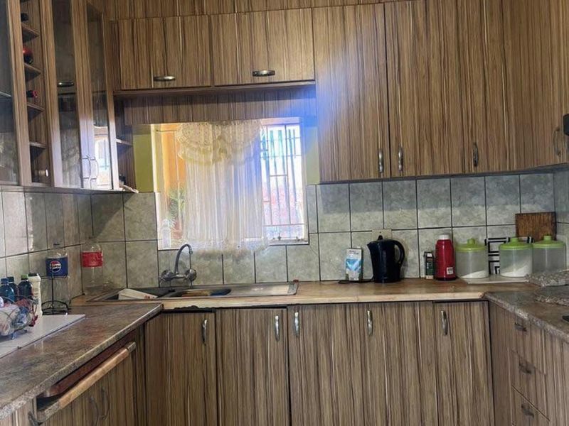 A functional kitchen featuring wood-grain laminate cabinetry, tiled backsplash, and a stainless steel sink with security bars on the window.