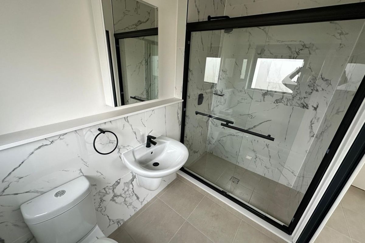 Modern bathroom featuring marble-look wall tiles, a glass-enclosed shower with black fixtures, a wall-mounted basin, and a sleek toilet.
