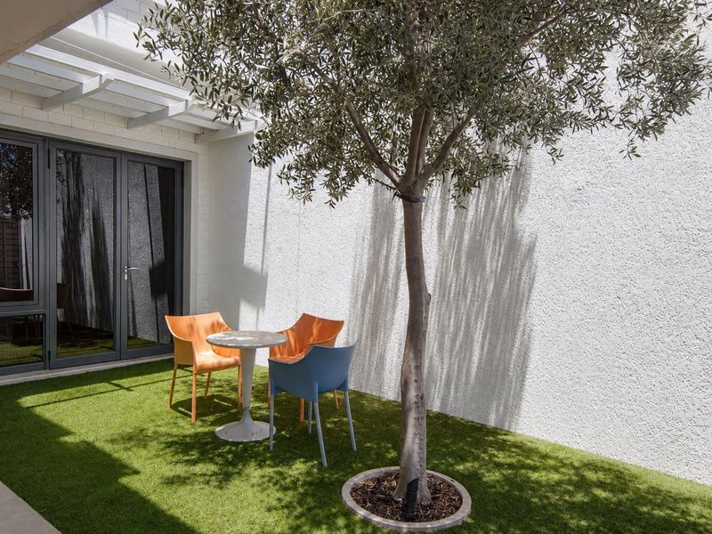 A private outdoor patio area featuring artificial turf, a mature tree, and modern aluminium-framed glass doors leading into the home.