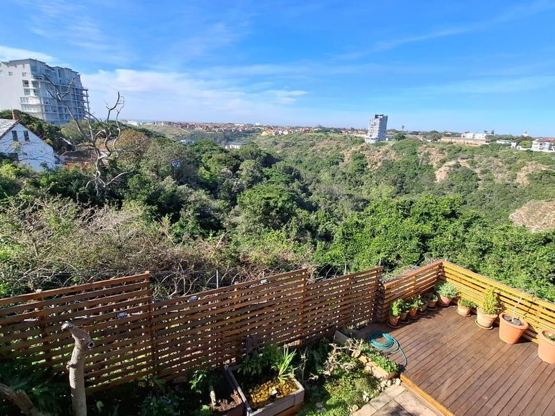 An elevated outdoor balcony featuring timber decking and a privacy screen, offering expansive views over the surrounding natural landscape.