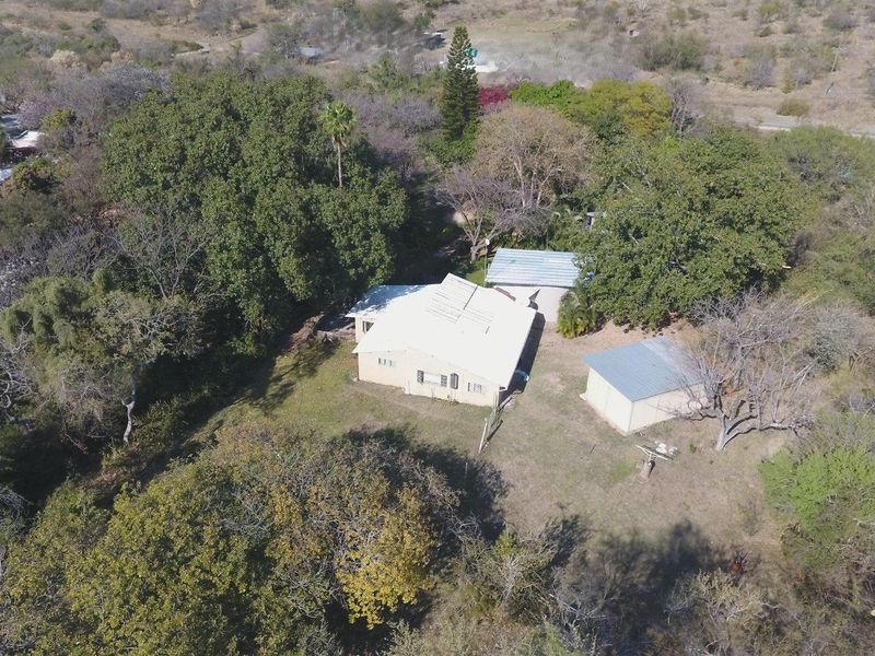 Aerial view of a farm property featuring a main dwelling and multiple outbuildings situated within a large, tree-lined plot.