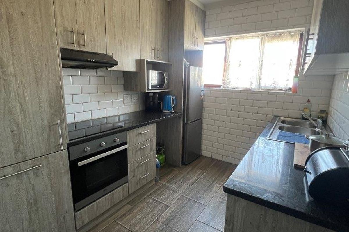 A functional kitchen featuring wood-look cabinetry, dark stone countertops, subway tile backsplash, and tiled flooring with integrated oven and extractor fan.