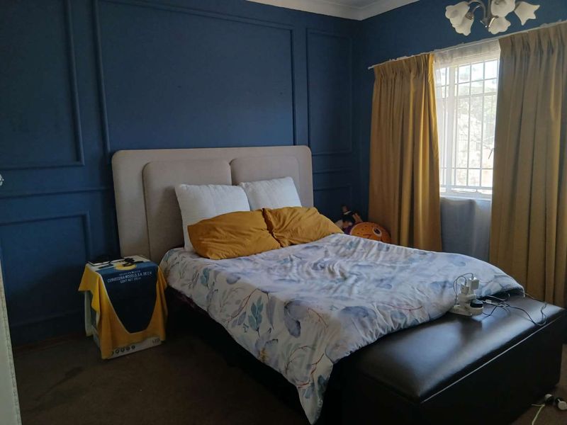A bedroom featuring dark blue accent walls with decorative wainscoting and a window fitted with security bars.