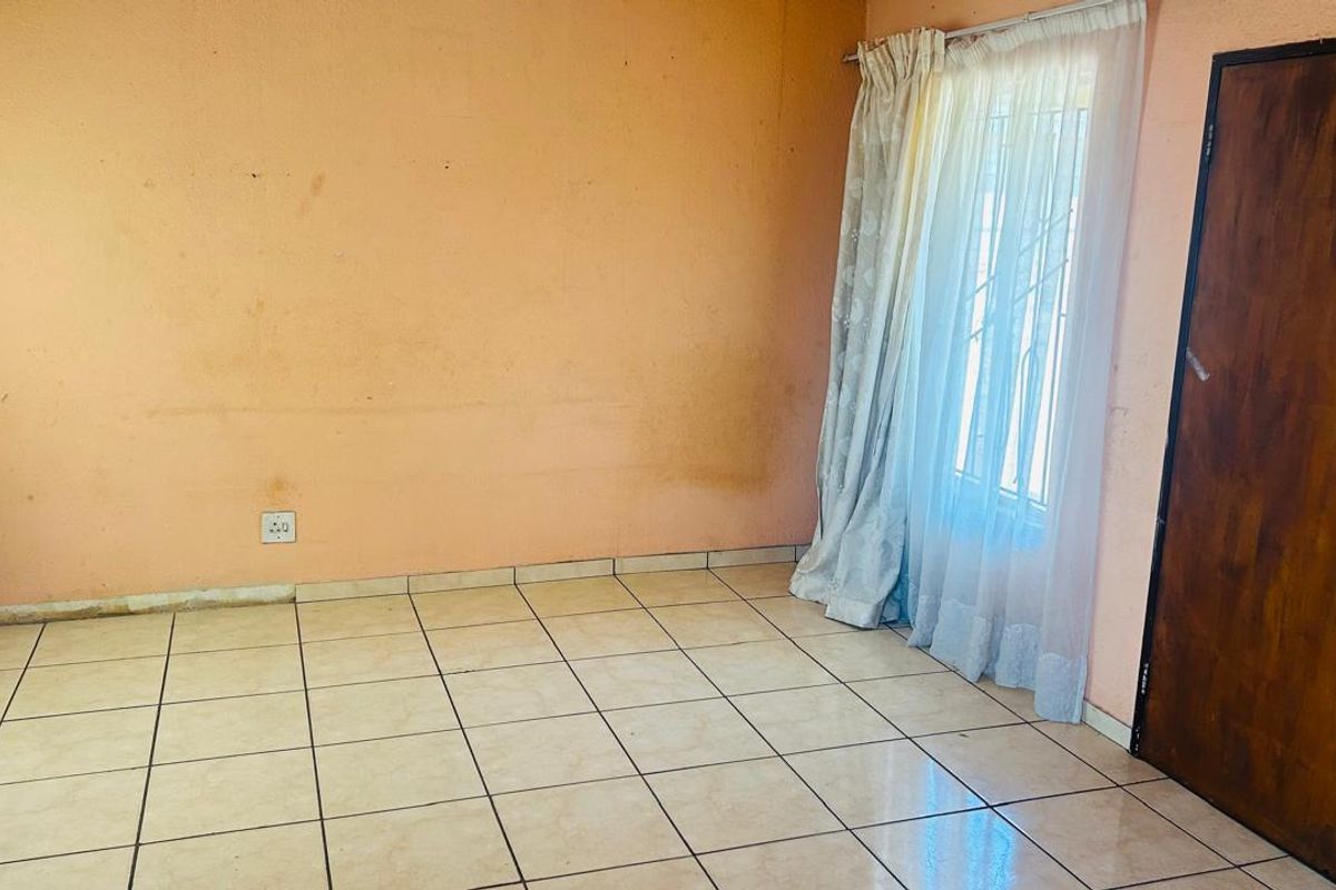 A vacant bedroom featuring tiled flooring, a single window with curtain tracks, and a wooden door.