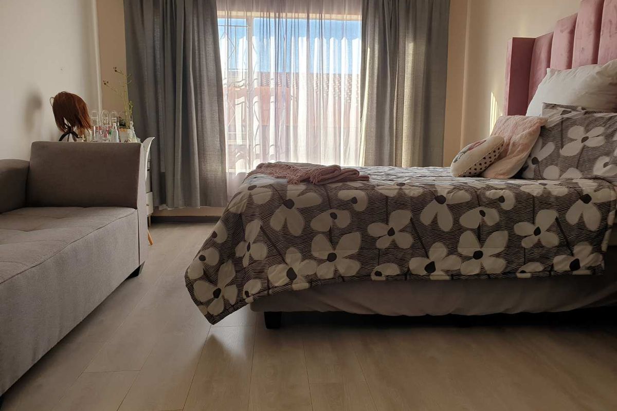 A well-lit bedroom featuring light-toned laminate flooring and large windows with curtain rails, providing a comfortable and functional living space.