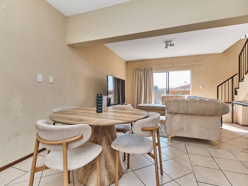 Open-plan living and dining area featuring tiled flooring, a staircase with metal railing, and a sliding glass door leading to the exterior.