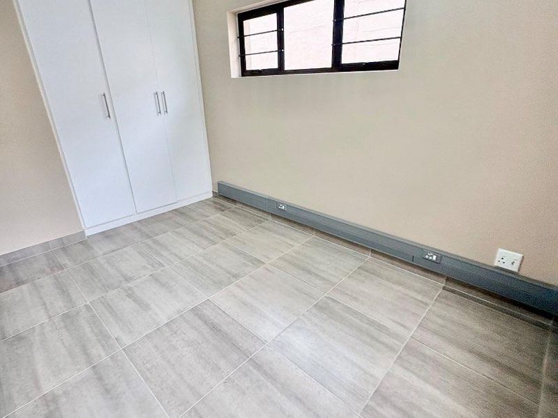 A clean, empty office space featuring modern grey tiled flooring, built-in white cupboards, and integrated electrical trunking for convenient workstation connectivity.