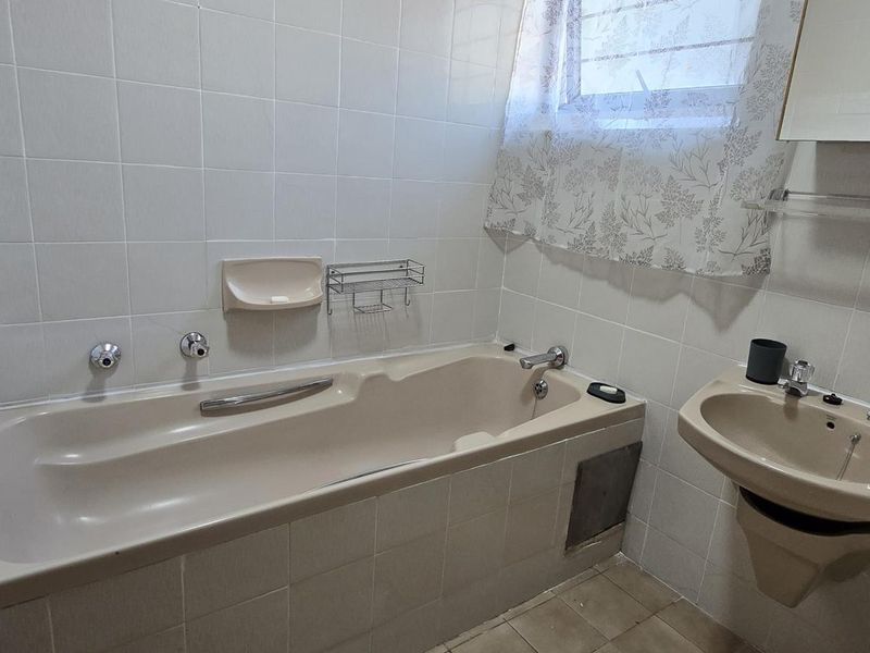 A functional bathroom featuring a built-in bathtub, wall-mounted basin, and tiled finishes, offering potential for modernization and cosmetic updates.