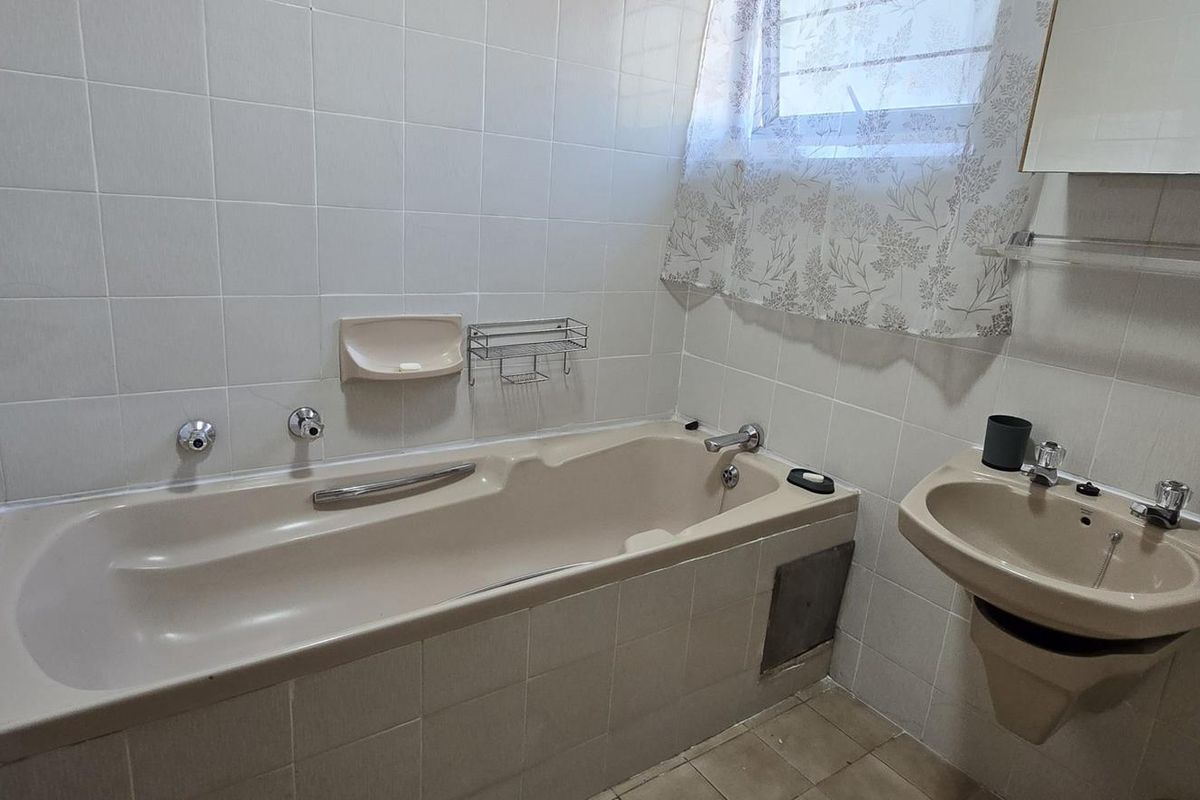 A functional bathroom featuring a built-in bathtub, wall-mounted basin, and tiled finishes, offering potential for modernization and cosmetic updates.