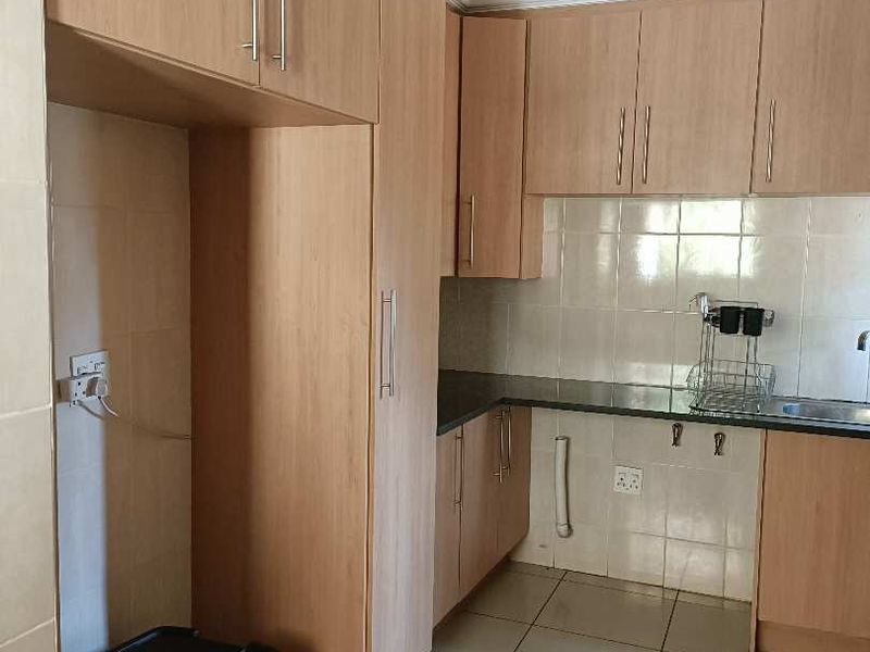 A functional kitchen featuring light wood-finish cabinetry, dark granite countertops, tiled backsplash, and ceramic floor tiles, offering a clean and practical workspace.