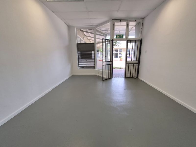 Empty retail entry space featuring a painted concrete floor, suspended ceiling, and secure metal gate entrance.
