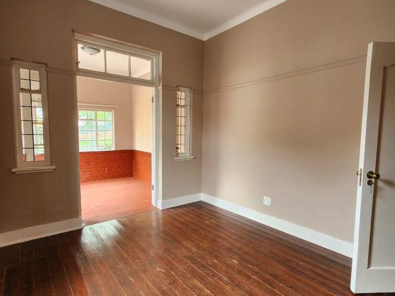 An empty bedroom featuring original hardwood flooring, timber-framed windows with transom detailing, and classic picture rails, offering a blank canvas for renovation.