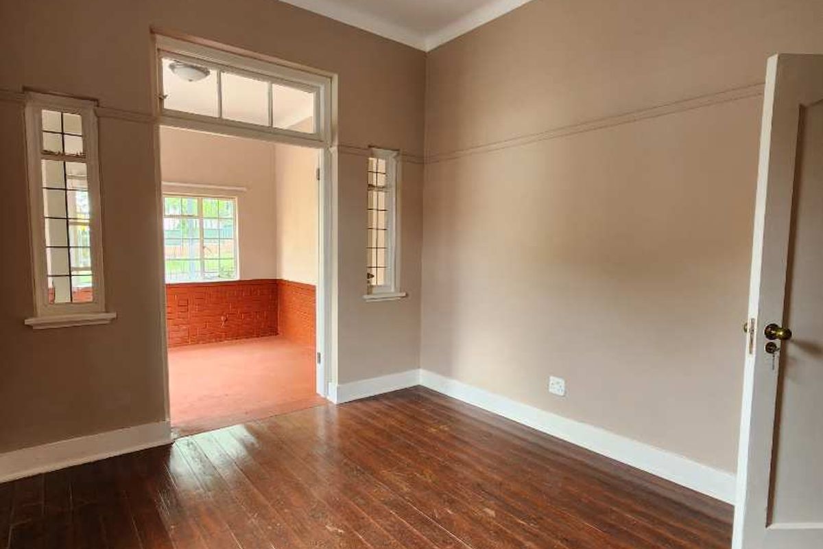 An empty bedroom featuring original hardwood flooring, timber-framed windows with transom detailing, and classic picture rails, offering a blank canvas for renovation.