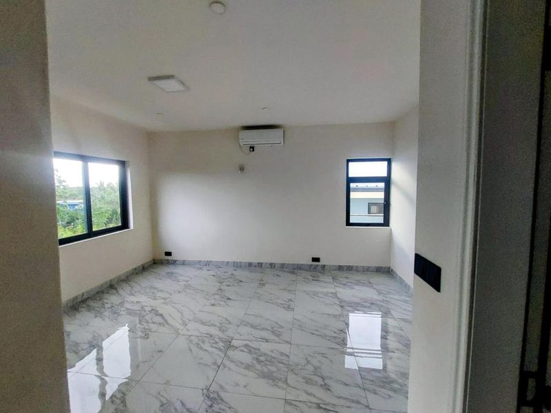 A bright, empty bedroom featuring polished marble-look floor tiles, modern black-framed windows, and a wall-mounted air conditioning unit.
