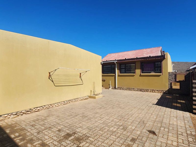 Rear exterior view of the property featuring a paved courtyard, rendered walls, and a tiled roof with security bars on the windows.