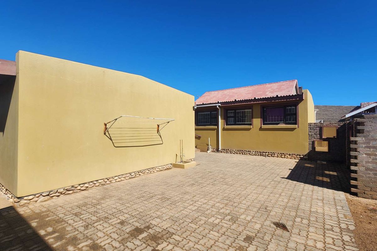 Rear exterior view of the property featuring a paved courtyard, rendered walls, and a tiled roof with security bars on the windows.