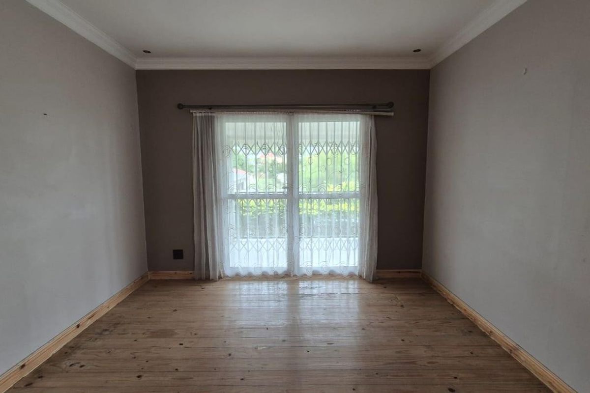 An empty bedroom featuring timber flooring, neutral wall tones, and a sliding glass door with integrated security gate leading to the exterior.