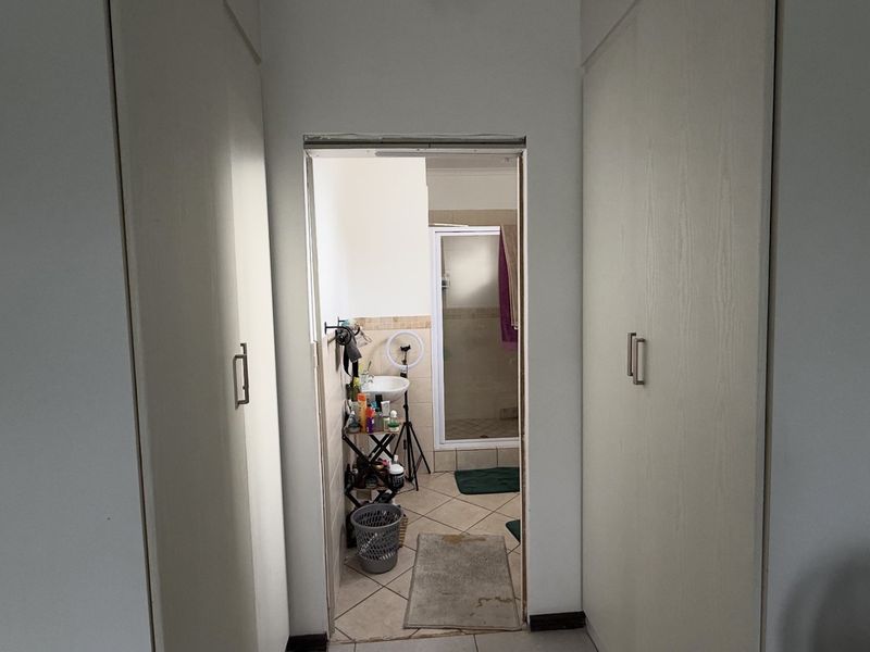A hallway featuring built-in cupboards leading into an en-suite bathroom area with tiled flooring.