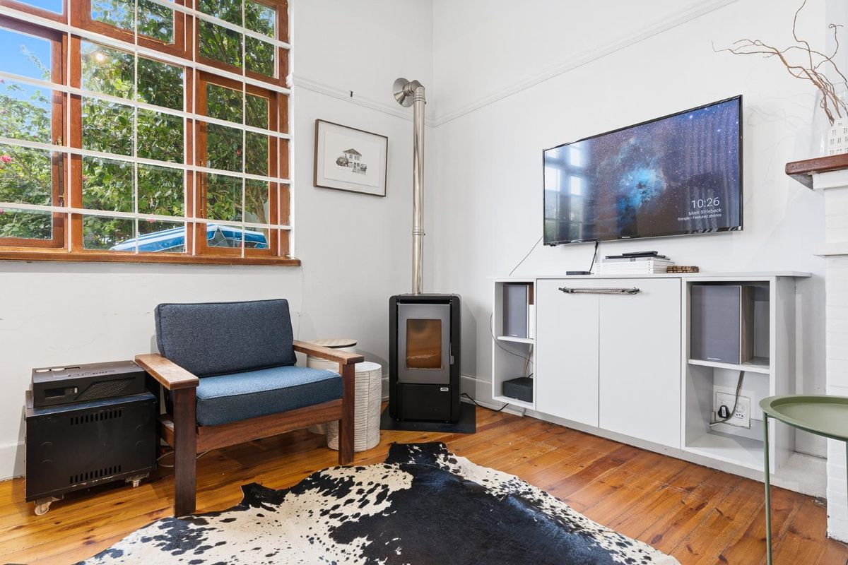 A cozy living room featuring original hardwood flooring, a wood-burning stove, and a large timber-framed sash window providing natural light.