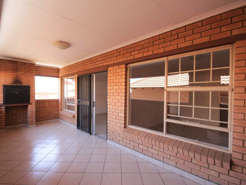 A spacious covered patio featuring exposed brick walls, tiled flooring, and a built-in braai, providing a functional outdoor entertainment area.