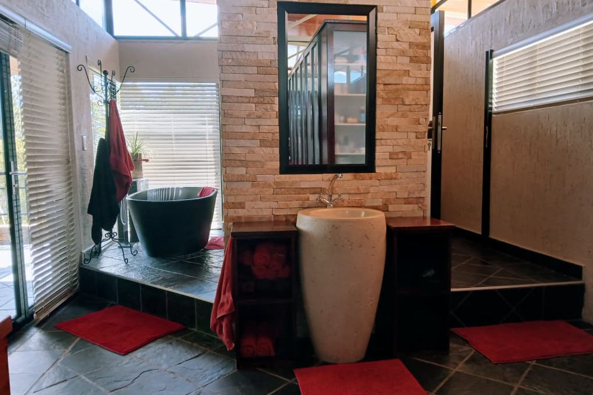 A unique bathroom featuring a stone-clad central pillar, a pedestal basin, and a freestanding bathtub set on a raised tiled platform.