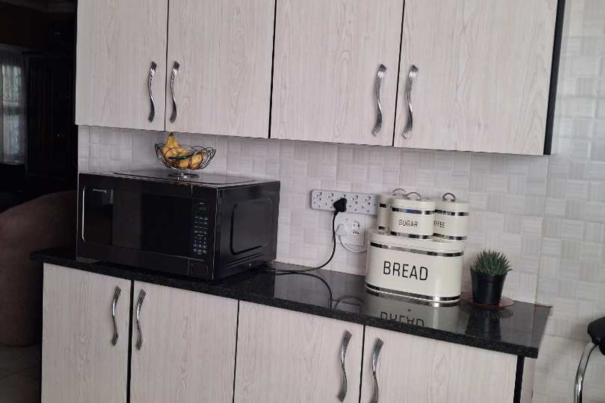 A functional kitchen area featuring light wood-grain cabinetry, dark granite countertops, and a tiled backsplash with integrated electrical points.