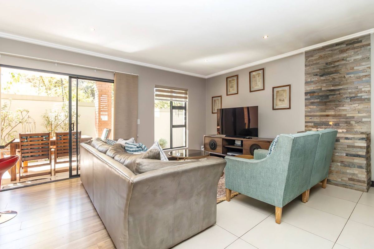 Spacious living room featuring a stone-clad fireplace, tiled and laminate flooring, and large sliding doors providing seamless access to the outdoor patio area.