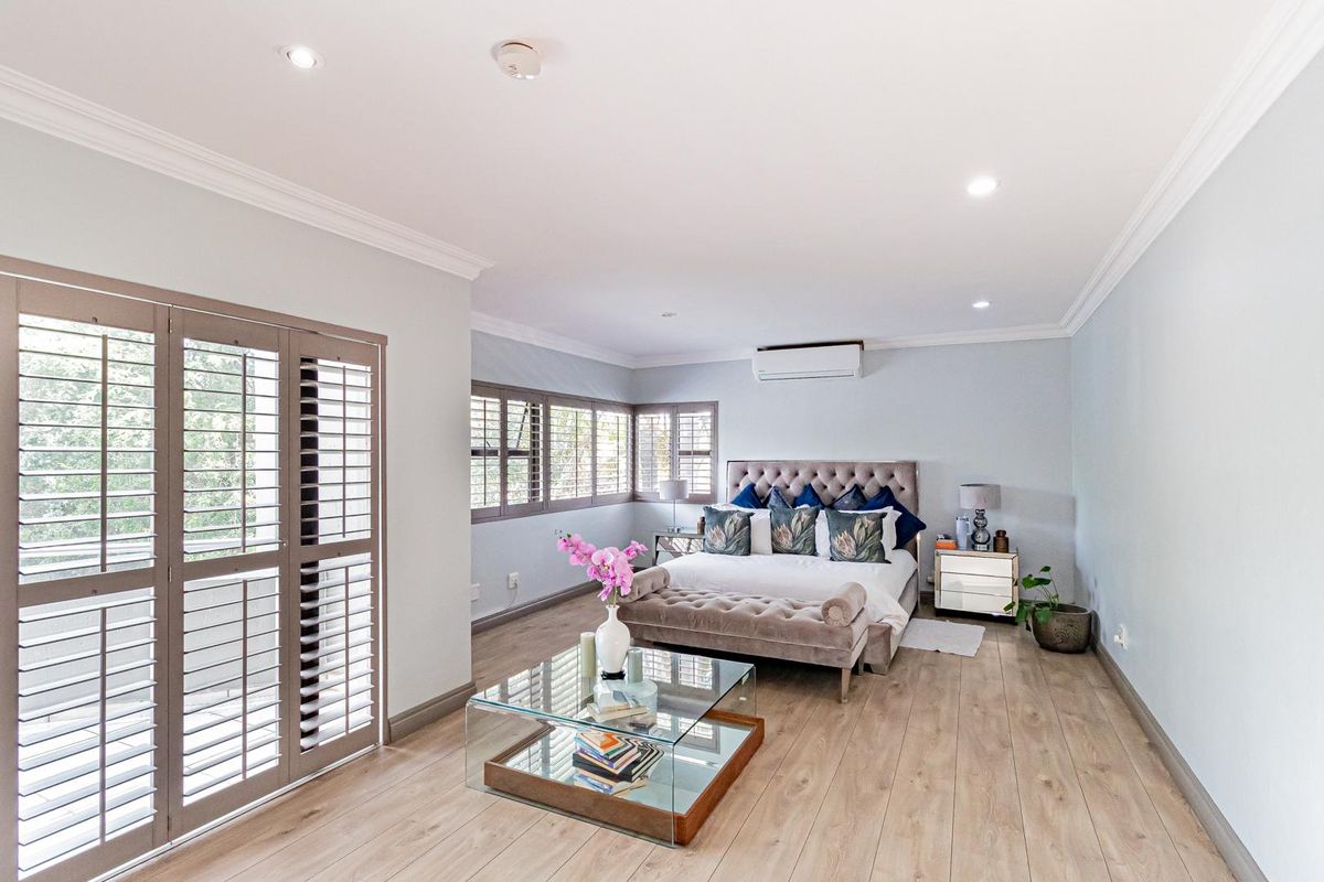 Spacious bedroom featuring light wood-look flooring, recessed ceiling lighting, crown molding, plantation shutters, and a wall-mounted air conditioning unit.