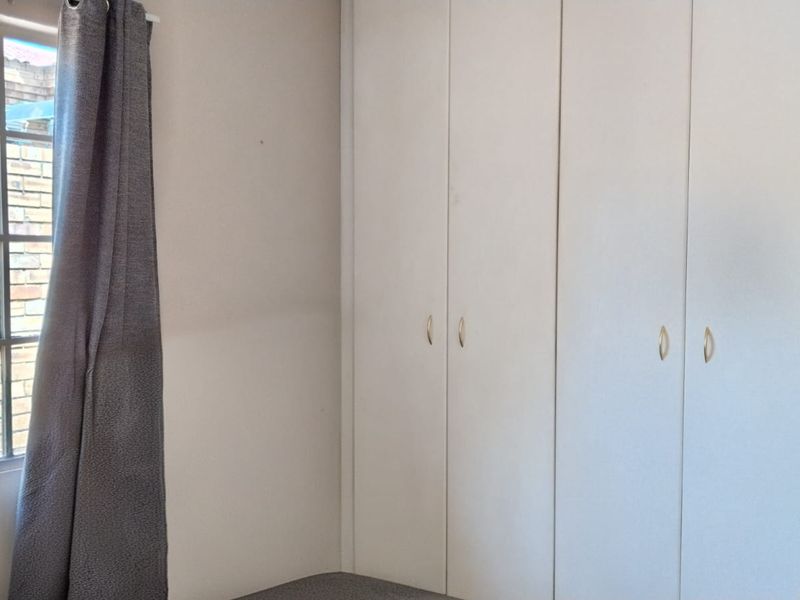 A clean, empty bedroom featuring built-in cupboards and a steel-framed window, offering a neutral space ready for personalization.