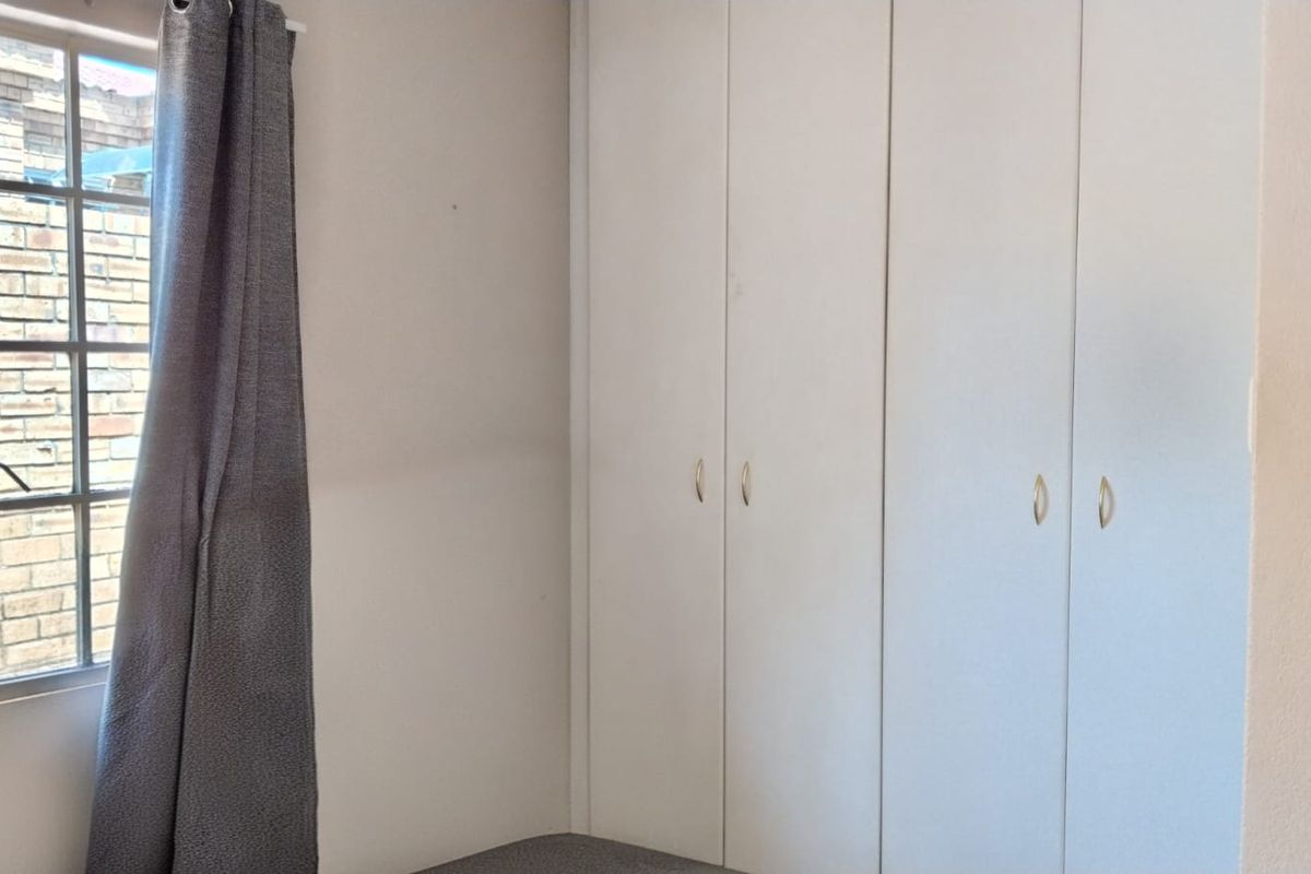 A clean, empty bedroom featuring built-in cupboards and a steel-framed window, offering a neutral space ready for personalization.