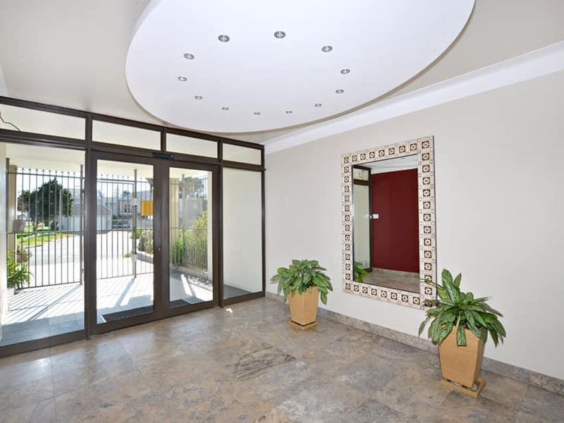 A bright and spacious apartment entrance foyer featuring tiled flooring, recessed ceiling lighting, and secure glass entrance doors.