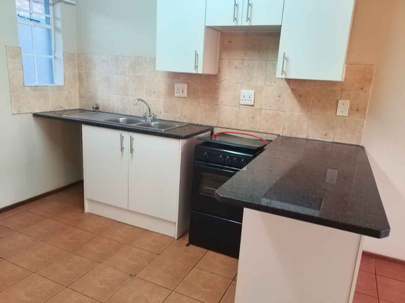 A functional kitchen featuring granite countertops, double sink, tiled backsplash, and white built-in cabinetry with ceramic floor tiles.