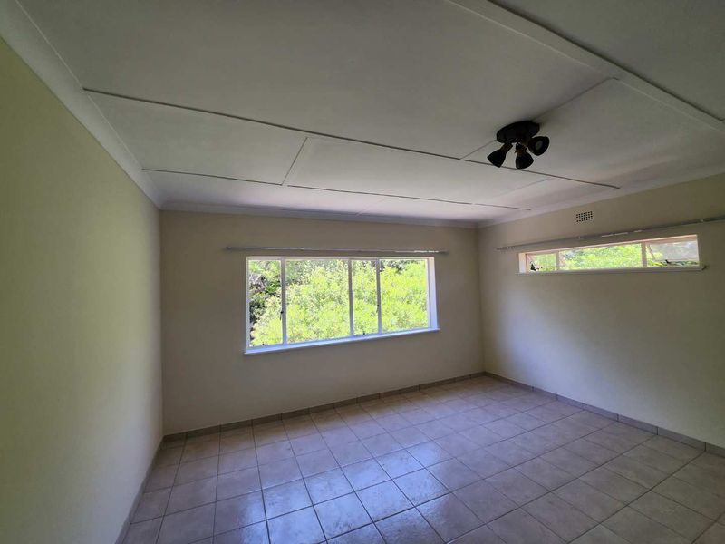 A spacious, empty bedroom featuring tiled flooring, large windows providing natural light, and a ceiling fan, ready for personalization.