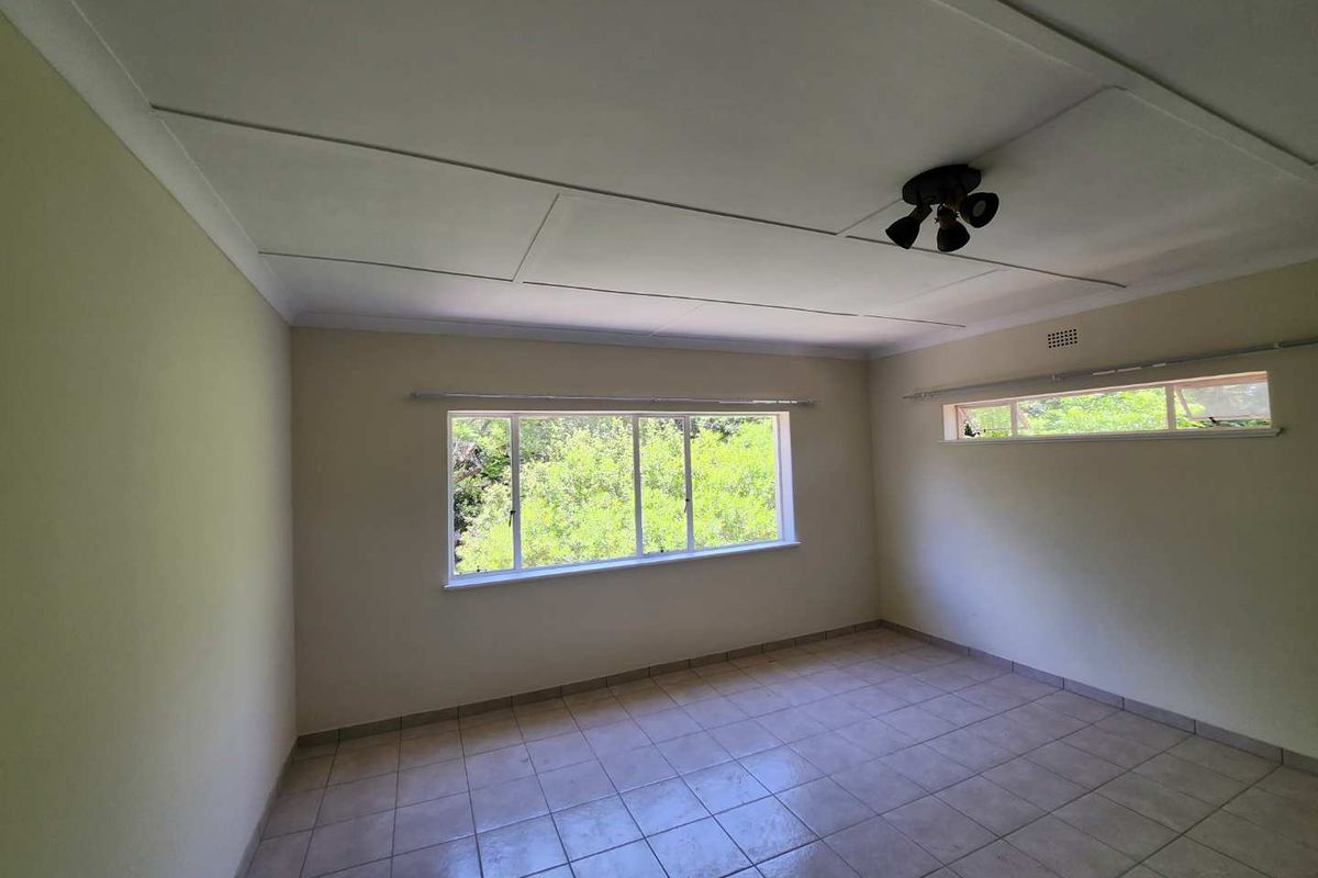 A spacious, empty bedroom featuring tiled flooring, large windows providing natural light, and a ceiling fan, ready for personalization.