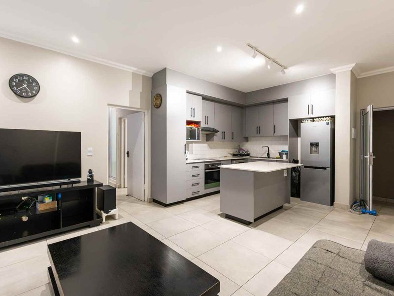 Modern open-plan living area featuring a contemporary kitchen with grey cabinetry, a central island, and sleek tiled flooring throughout the space.