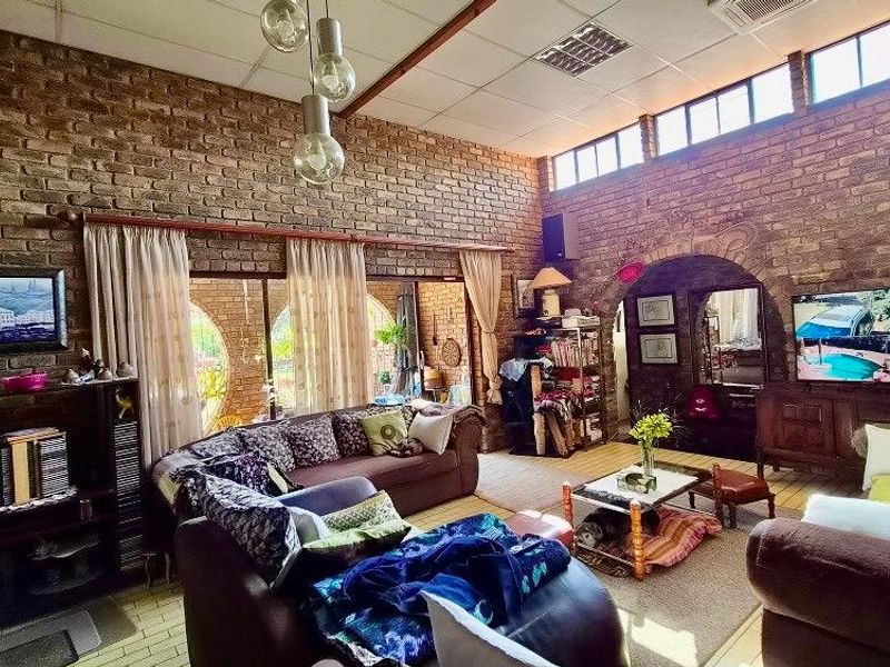 Spacious living room featuring rustic exposed brick walls, high ceilings with clerestory windows, and a distinctive arched architectural detail.