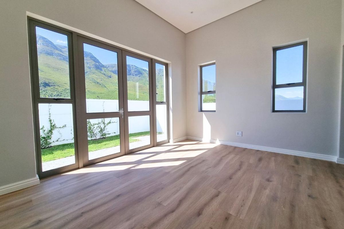 A bright, empty living room featuring modern wood-look flooring, neutral walls, and large glass sliding doors offering scenic mountain views.