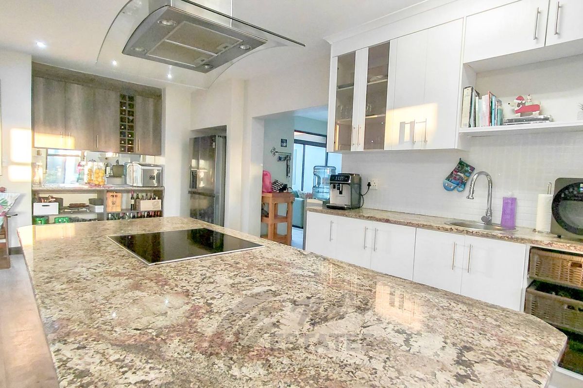 Modern kitchen featuring a large granite island with integrated induction hob, overhead extractor fan, white cabinetry, and stainless steel sink.