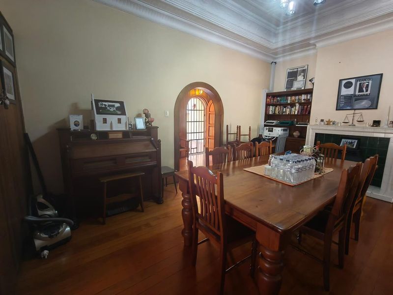 A formal dining room featuring hardwood flooring, ornate crown molding, a built-in fireplace, and an arched doorway leading to an adjacent space.