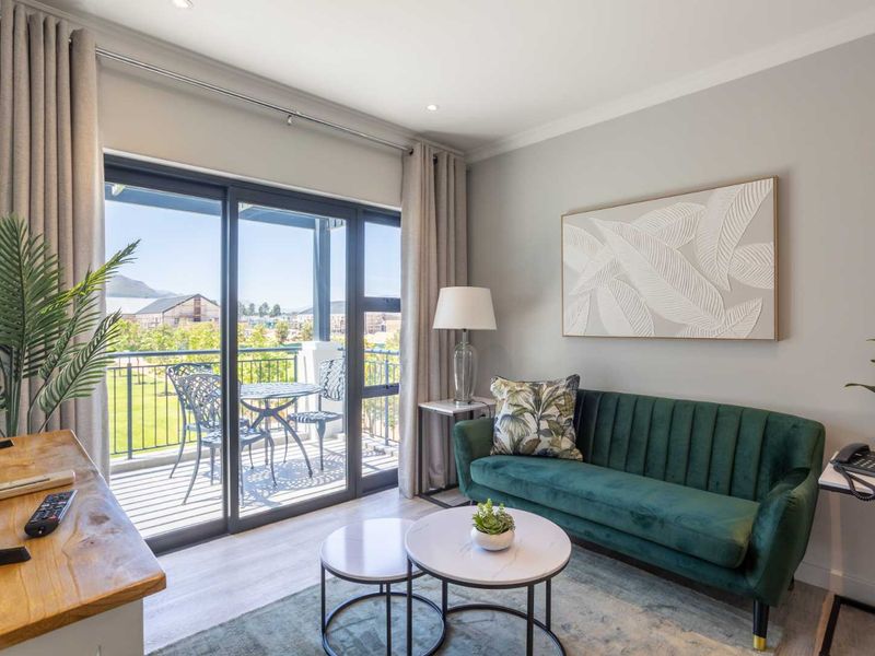 A bright and modern living room featuring laminate flooring, recessed lighting, and large sliding glass doors that open onto a private balcony.