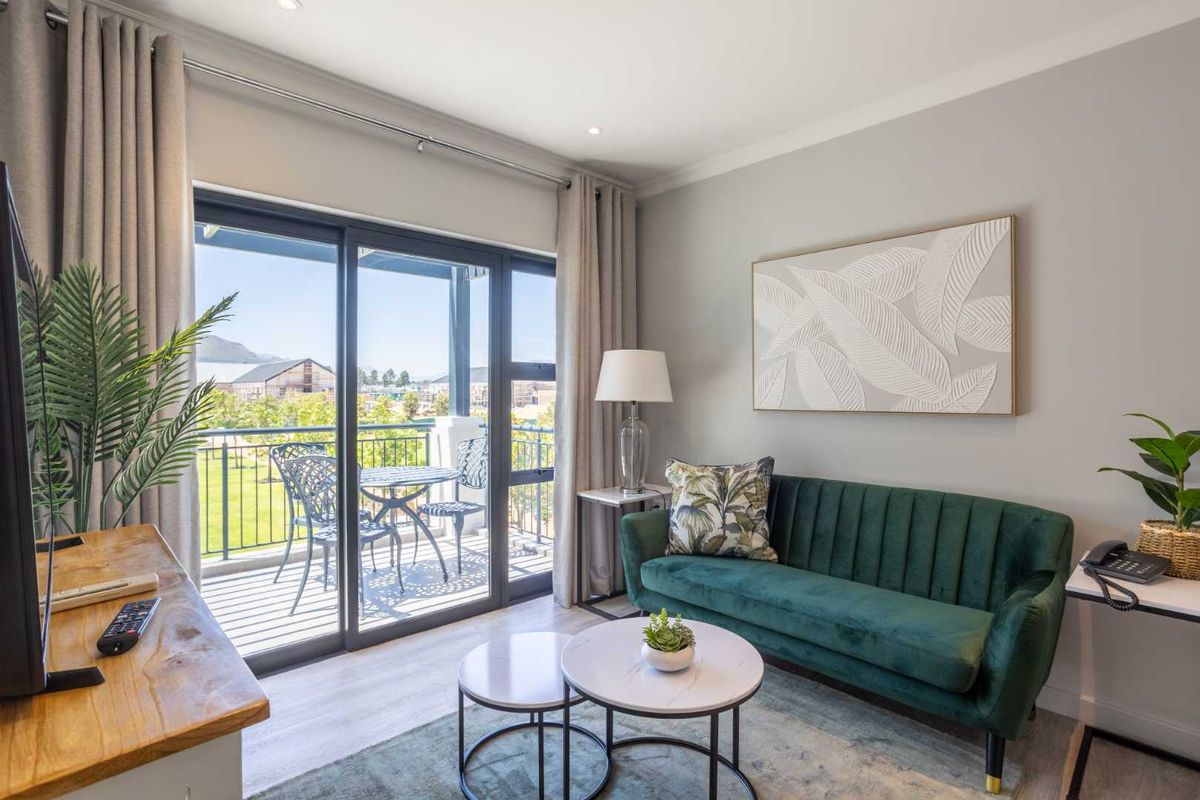A bright and modern living room featuring laminate flooring, recessed lighting, and large sliding glass doors that open onto a private balcony.