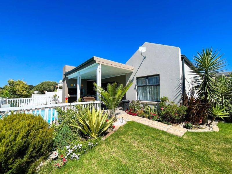 Rear exterior view featuring a covered patio, swimming pool, landscaped garden, and paved walkway, providing an inviting outdoor entertainment space.
