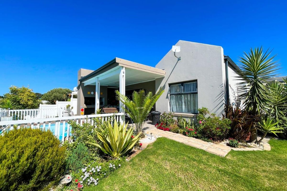 Rear exterior view featuring a covered patio, swimming pool, landscaped garden, and paved walkway, providing an inviting outdoor entertainment space.